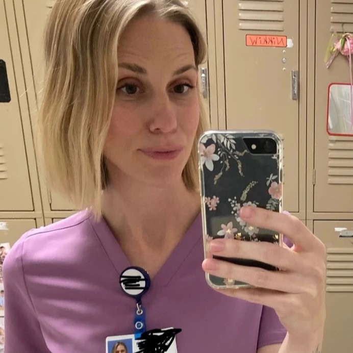 Person in purple scrubs taking a selfie in front of lockers.