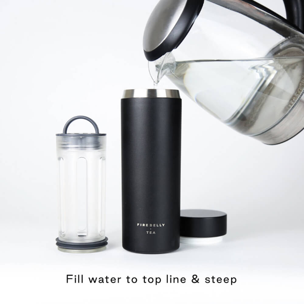 A person pours water from a glass kettle into a black Firebelly Tea travel mug with an infuser.