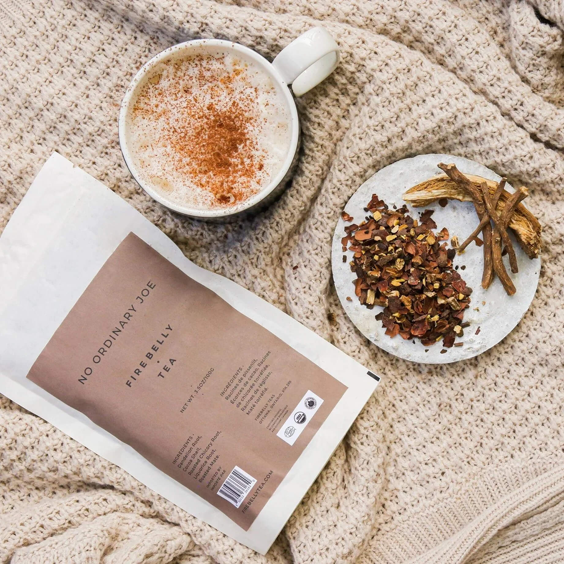 Cup of spiced latte, tea packet, and ingredients on a knitted blanket.