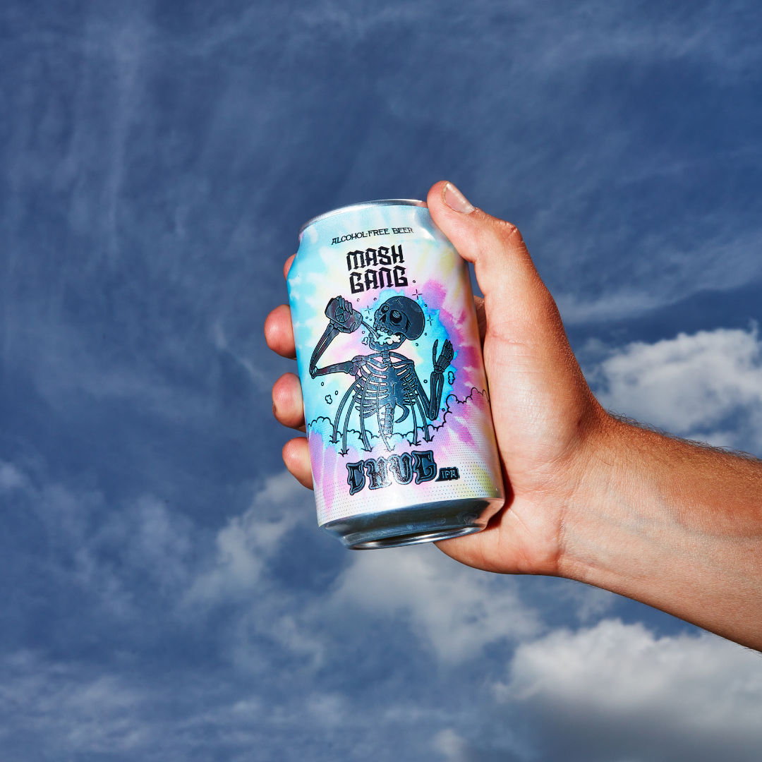 Hand holding a colorful can with skeleton artwork against a cloudy sky.