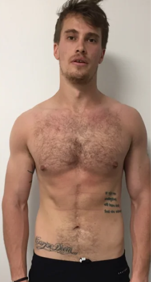 Shirtless man with tattoos on chest and abdomen, standing against a plain background.