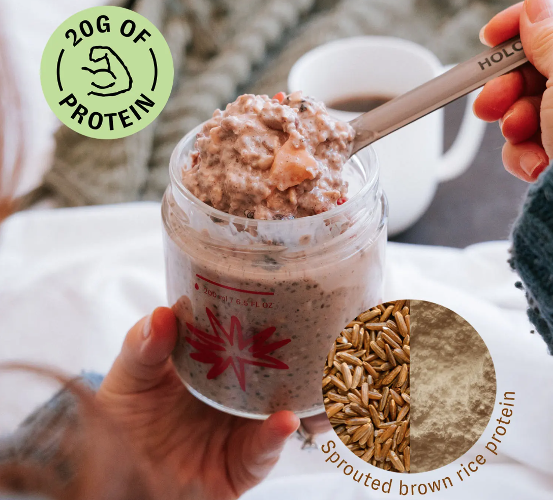 Person holding jar of oatmeal with spoon, coffee cup in background.