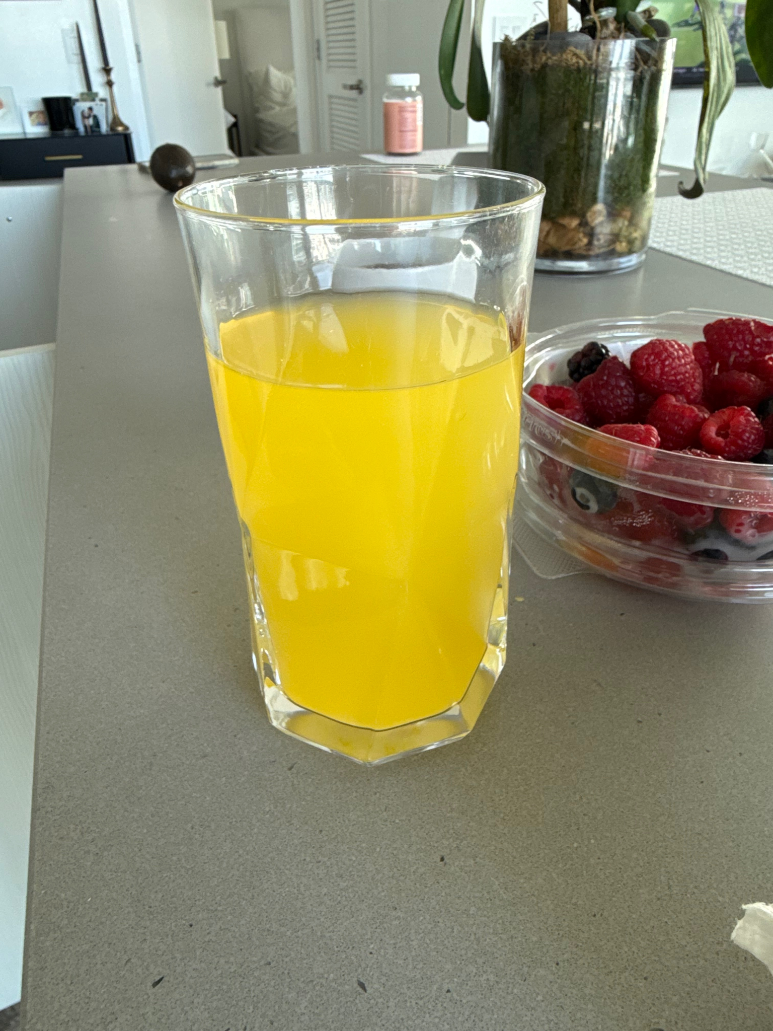A glass of orange juice and a bowl of mixed berries on a countertop.