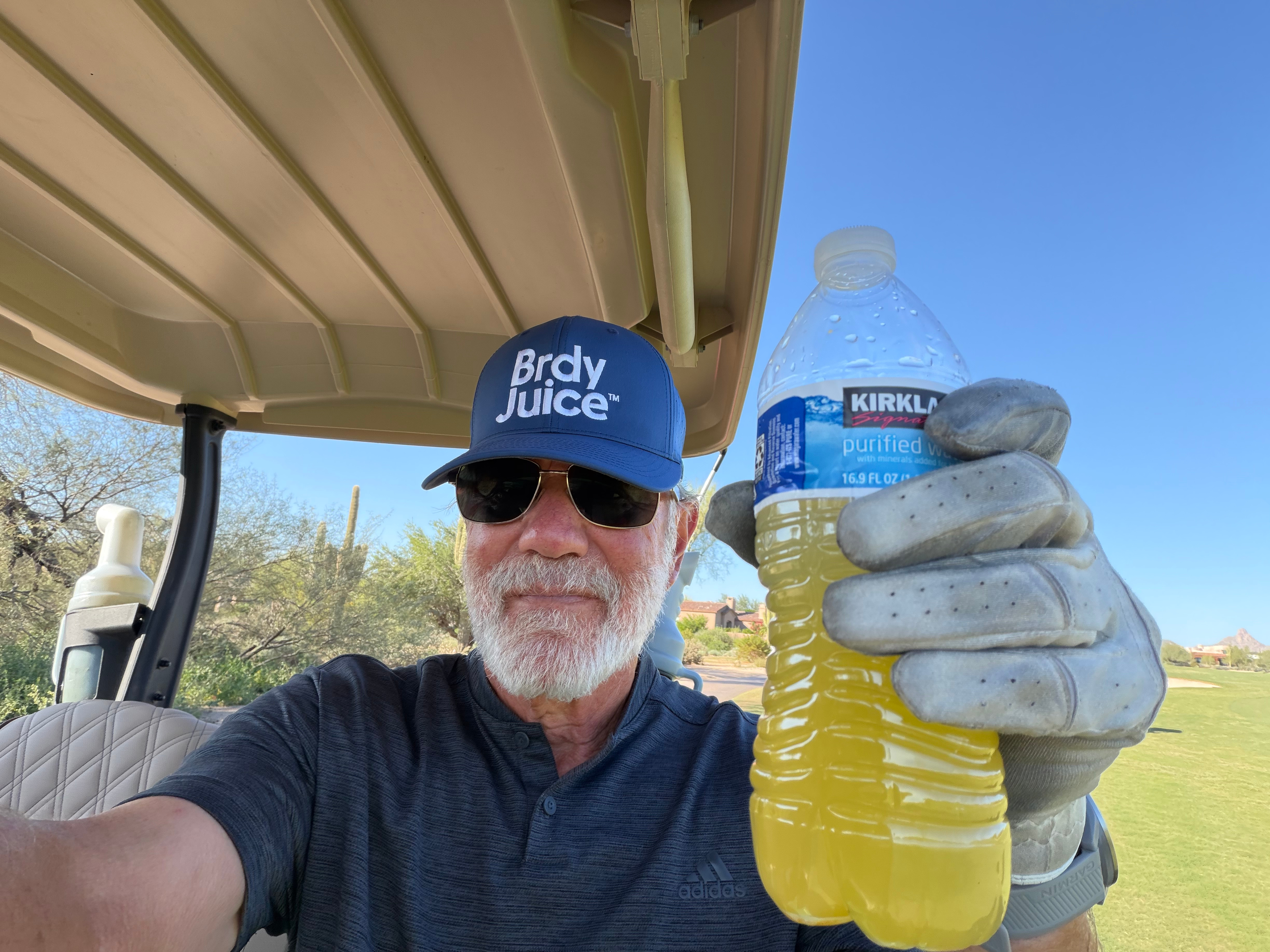 Person holding a tinted water bottle in a golf cart, wearing a blue cap and gloves.