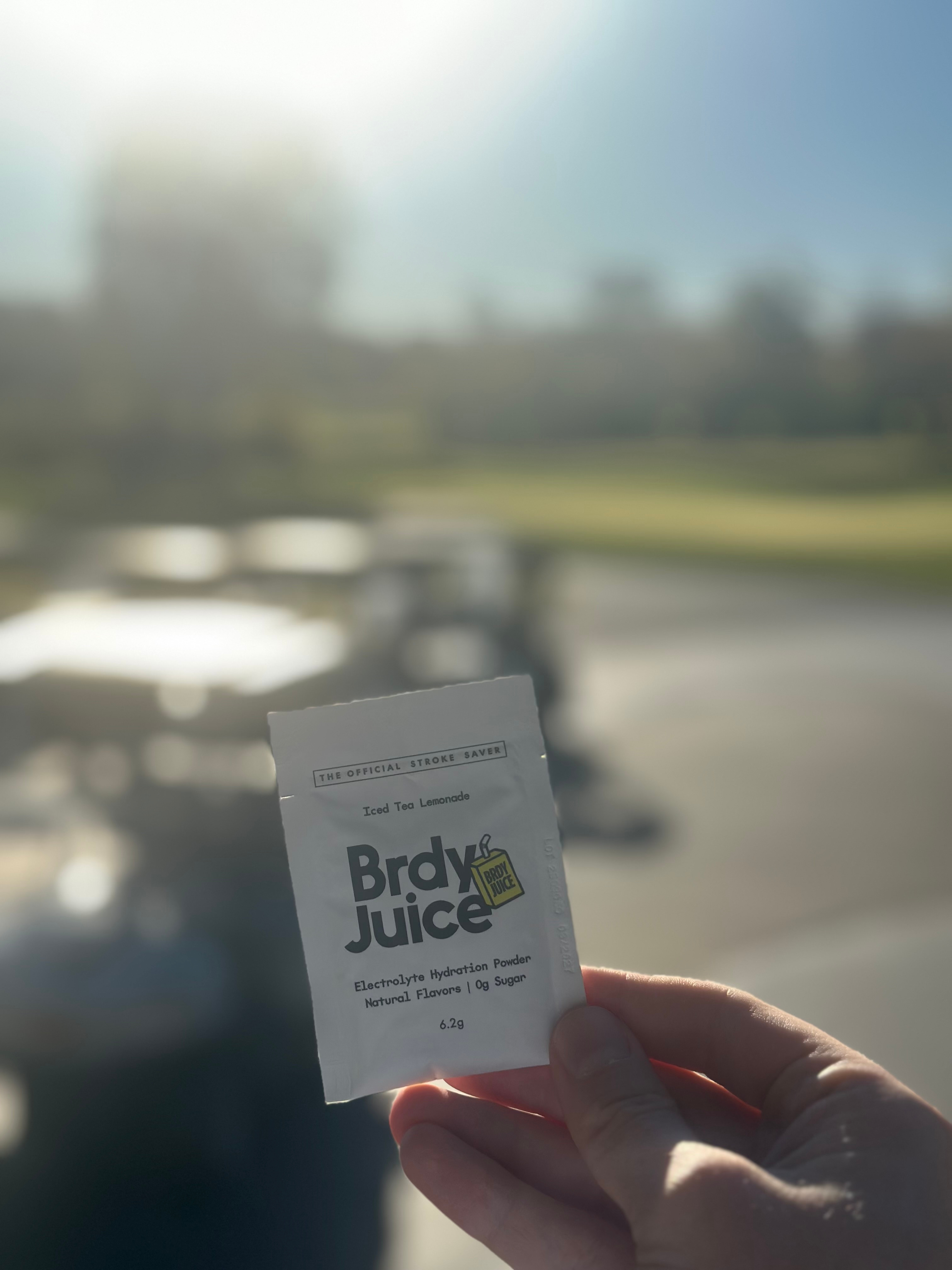 Hand holding a packet of Brady Juice hydration powder in a sunny outdoor setting.