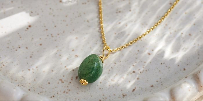 Green stone pendant on a gold chain placed on a speckled surface.