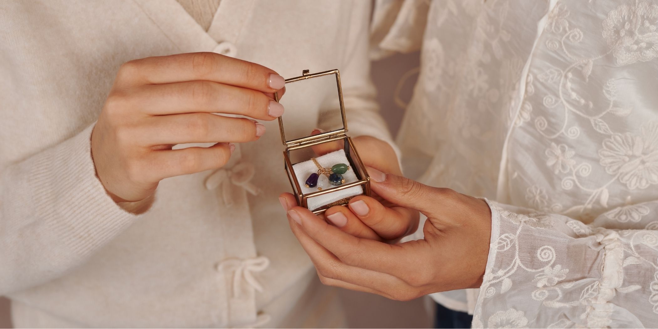 Two people holding a jewelry box with gemstone pendants.