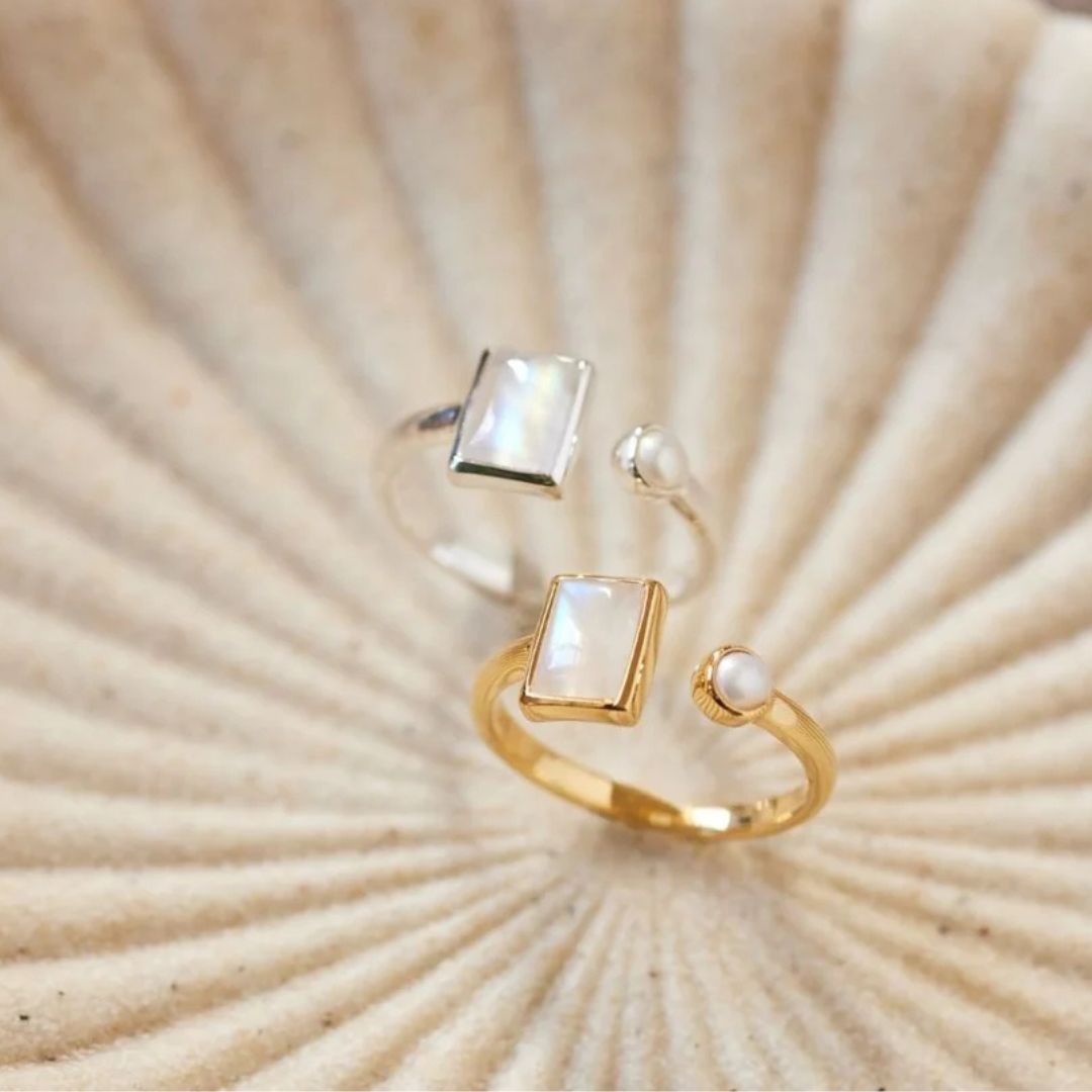 Two rings with rectangular and round stones on a shell background.