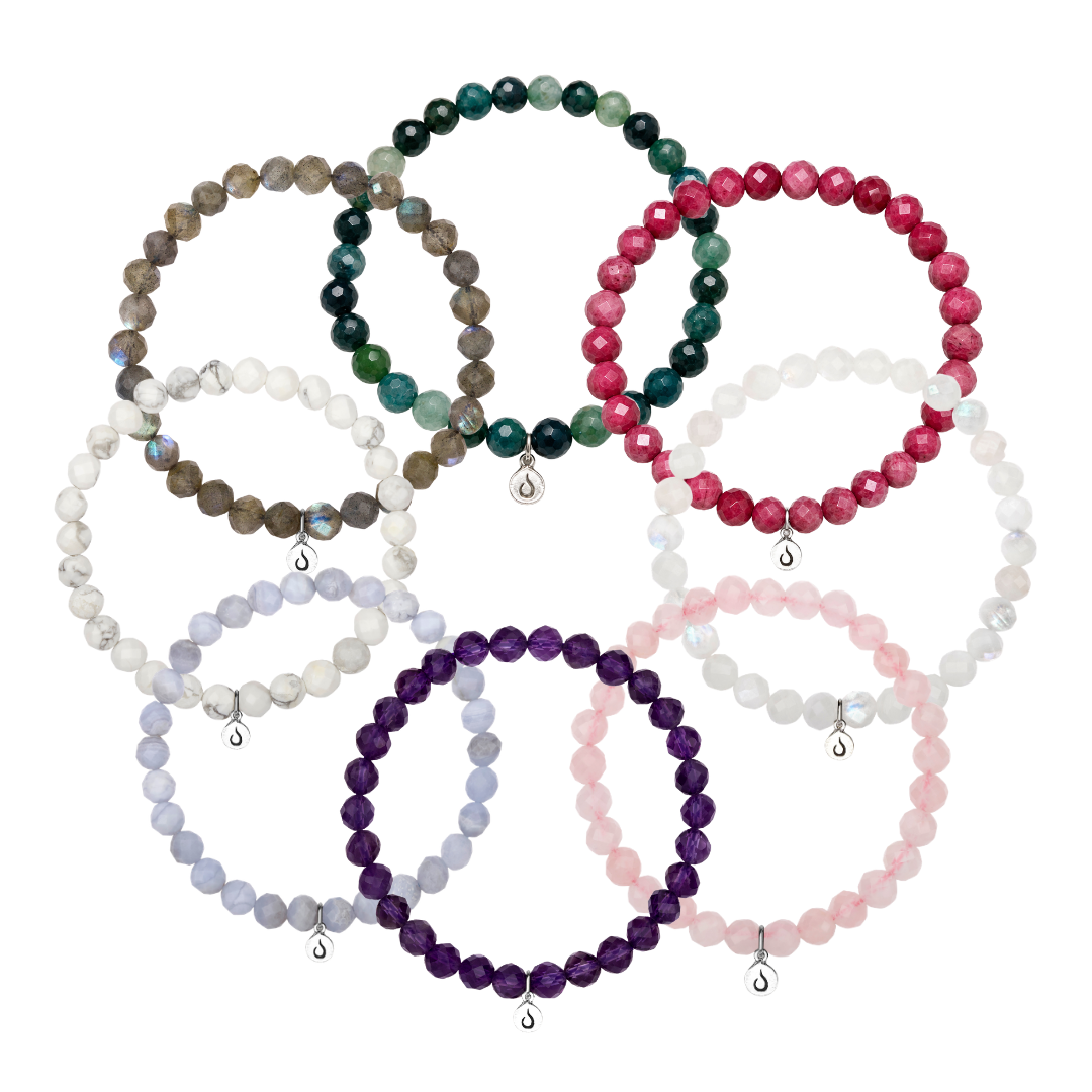 Nine colorful beaded bracelets with charms arranged in a circular pattern on a white background.