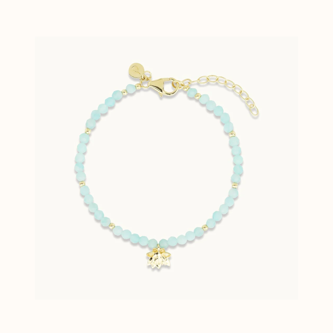 A beaded bracelet with turquoise beads and a gold charm on a white background.
