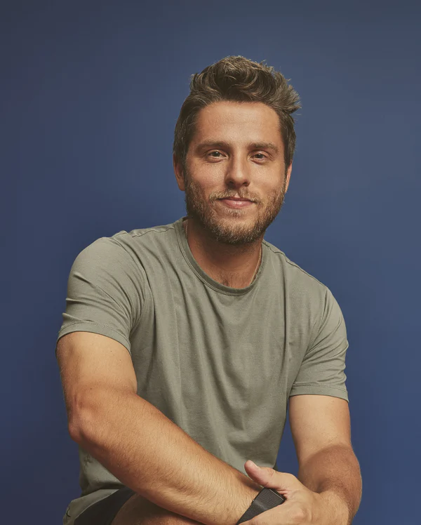 Man with a beard and short hair, wearing a gray t-shirt, against a blue background.