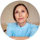Person in a light blue blouse looking at the camera, seated indoors.
