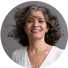 Smiling person with shoulder-length gray hair and wearing a white shirt.