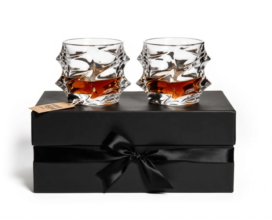 Two textured glasses with amber liquid on a black gift box with a ribbon.