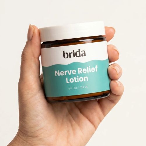 A hand holds a jar of Brida Nerve Relief Lotion against a plain, light-colored background.