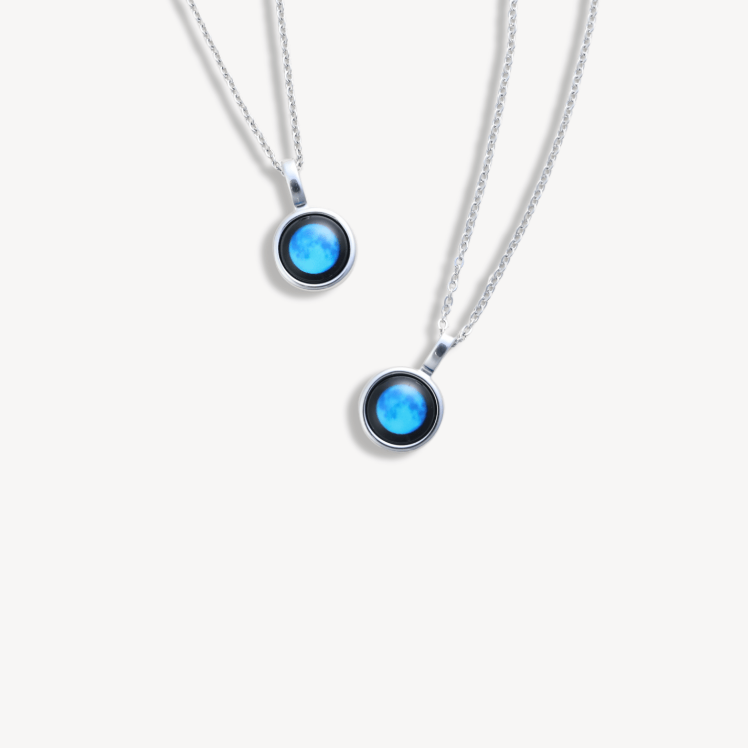 Two silver necklaces with round blue pendants on a white background.
