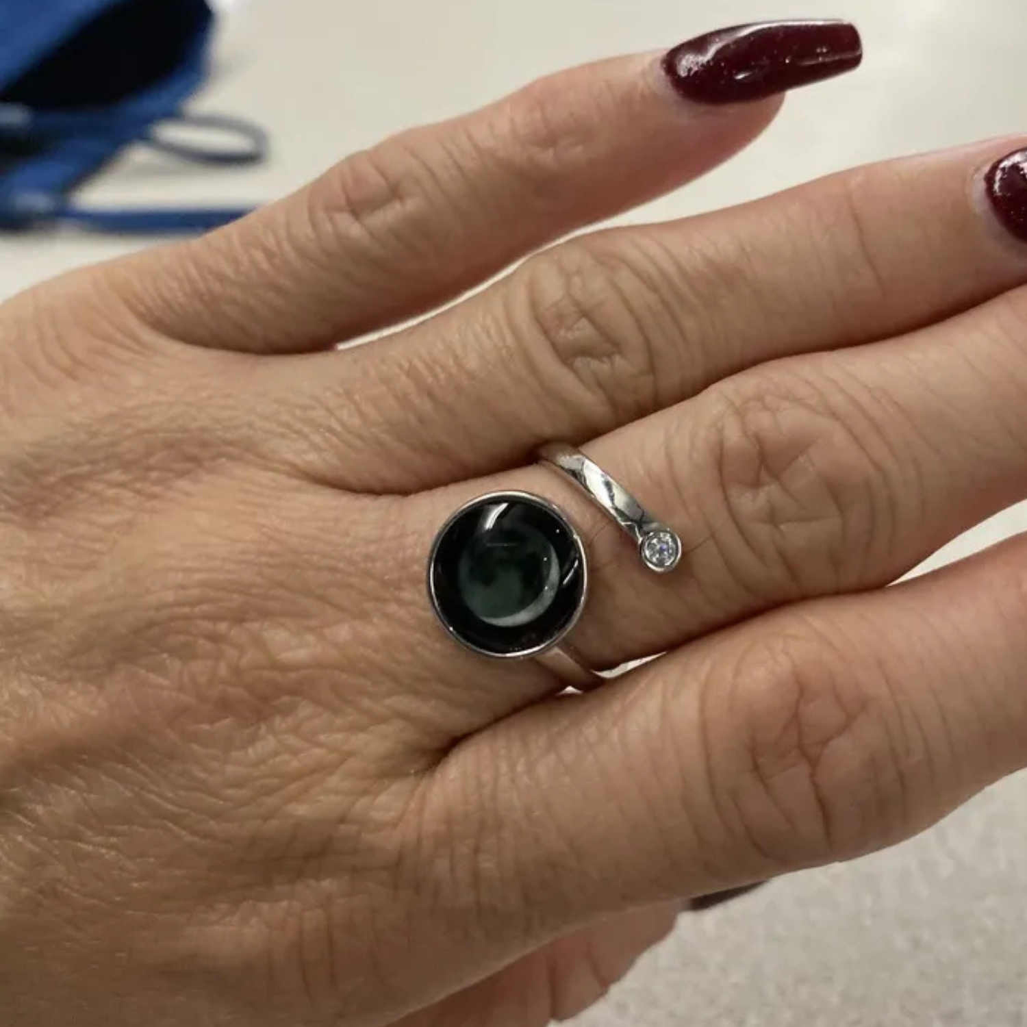 A hand with a silver ring featuring a black stone and small diamond accent.