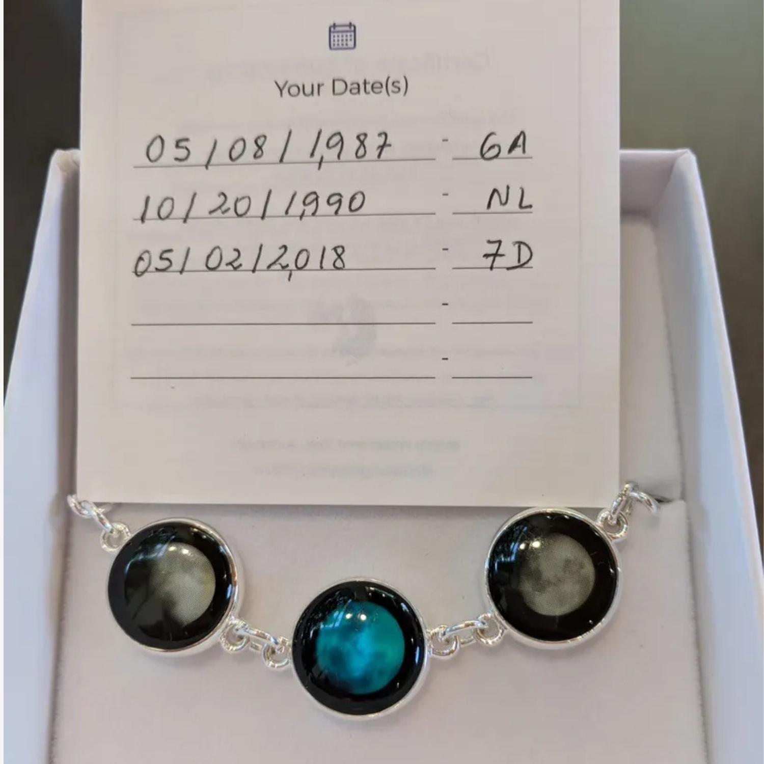 Necklace with circular pendants displayed alongside handwritten date notes in a gift box.