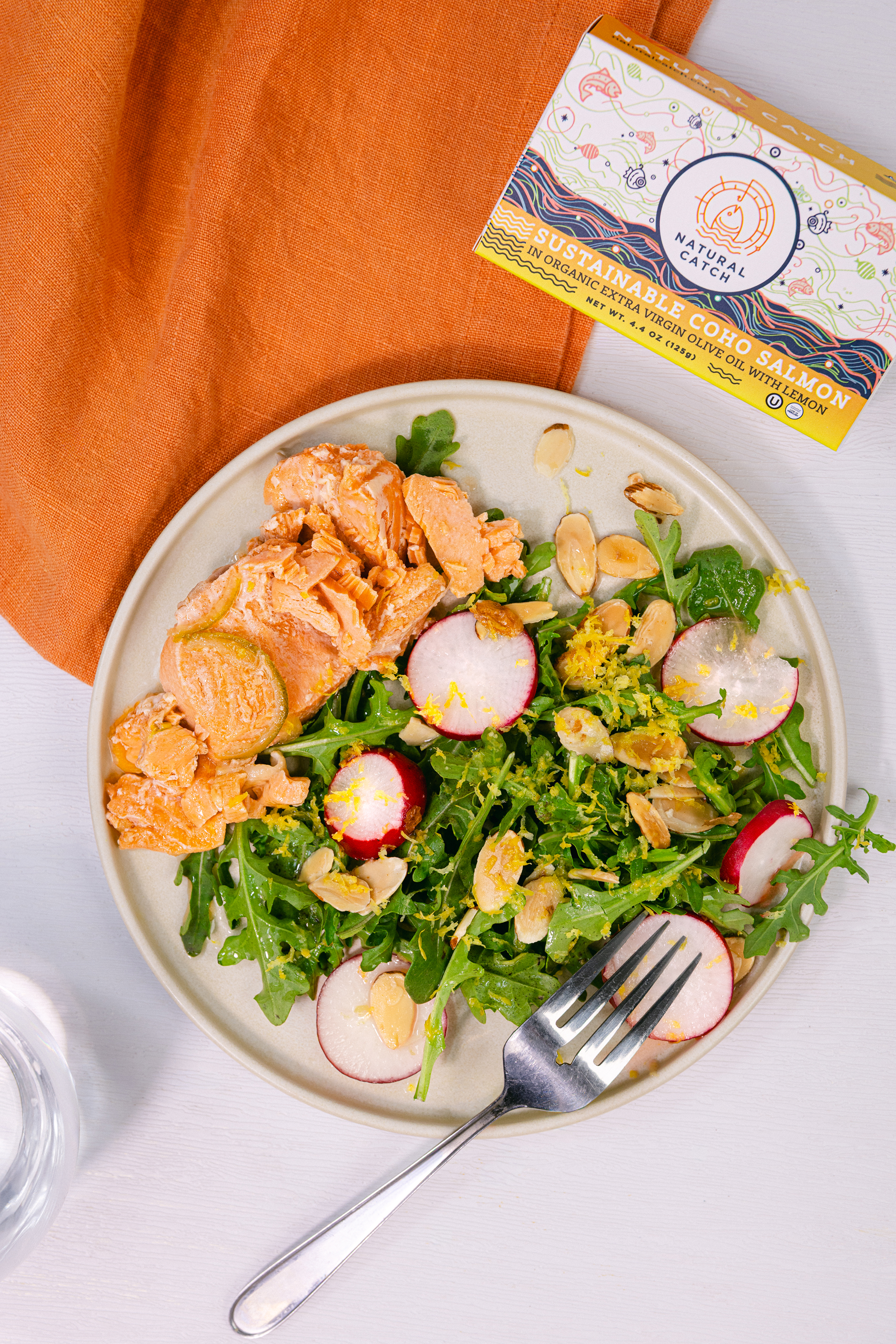 A top-down view of a salmon salad with radishes and almonds, with a box of salmon nearby.