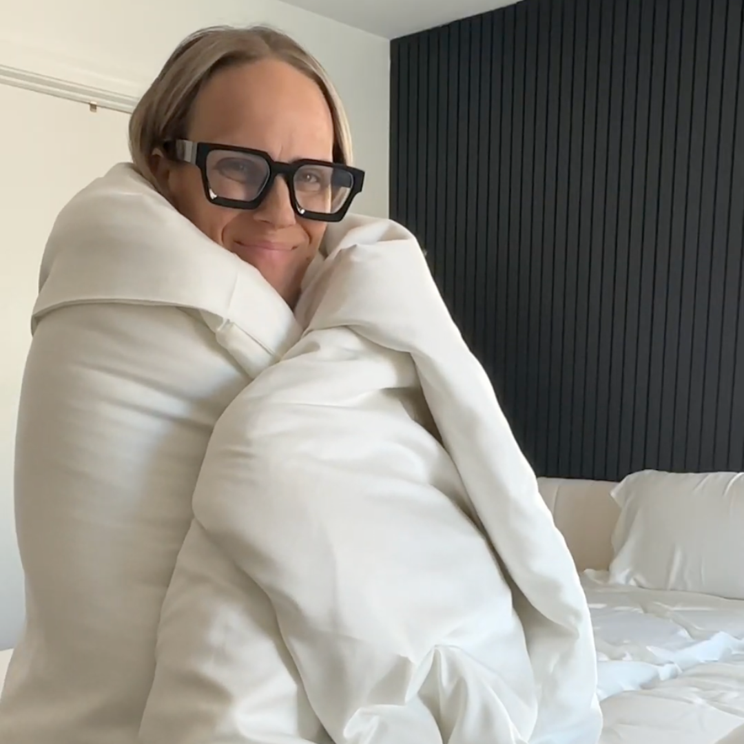 Person wrapped in a white comforter, smiling, wearing black glasses.