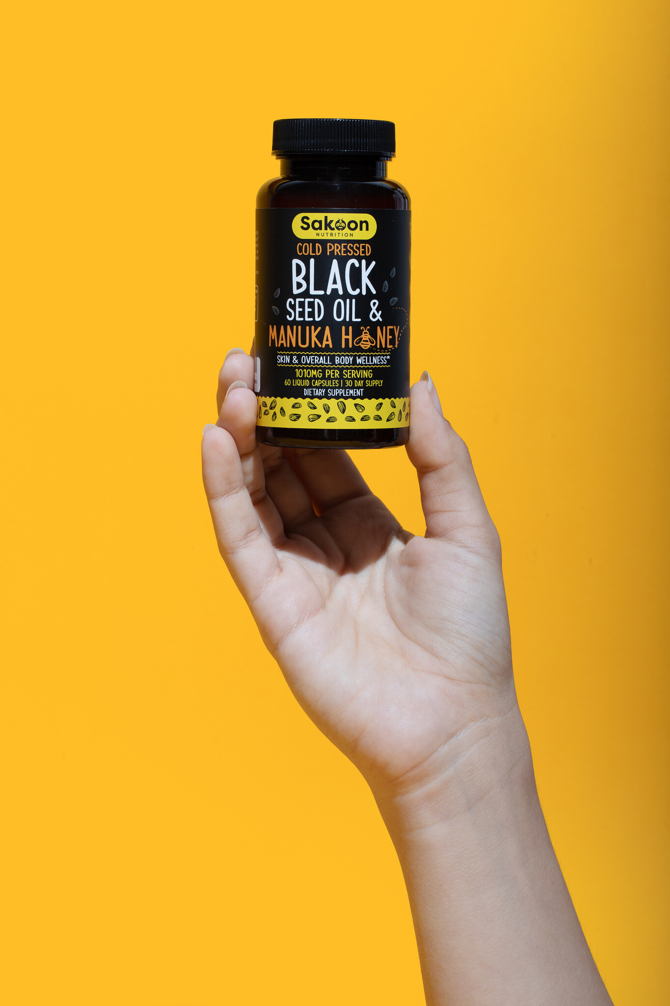Hand holding a bottle of black seed oil against a yellow background.