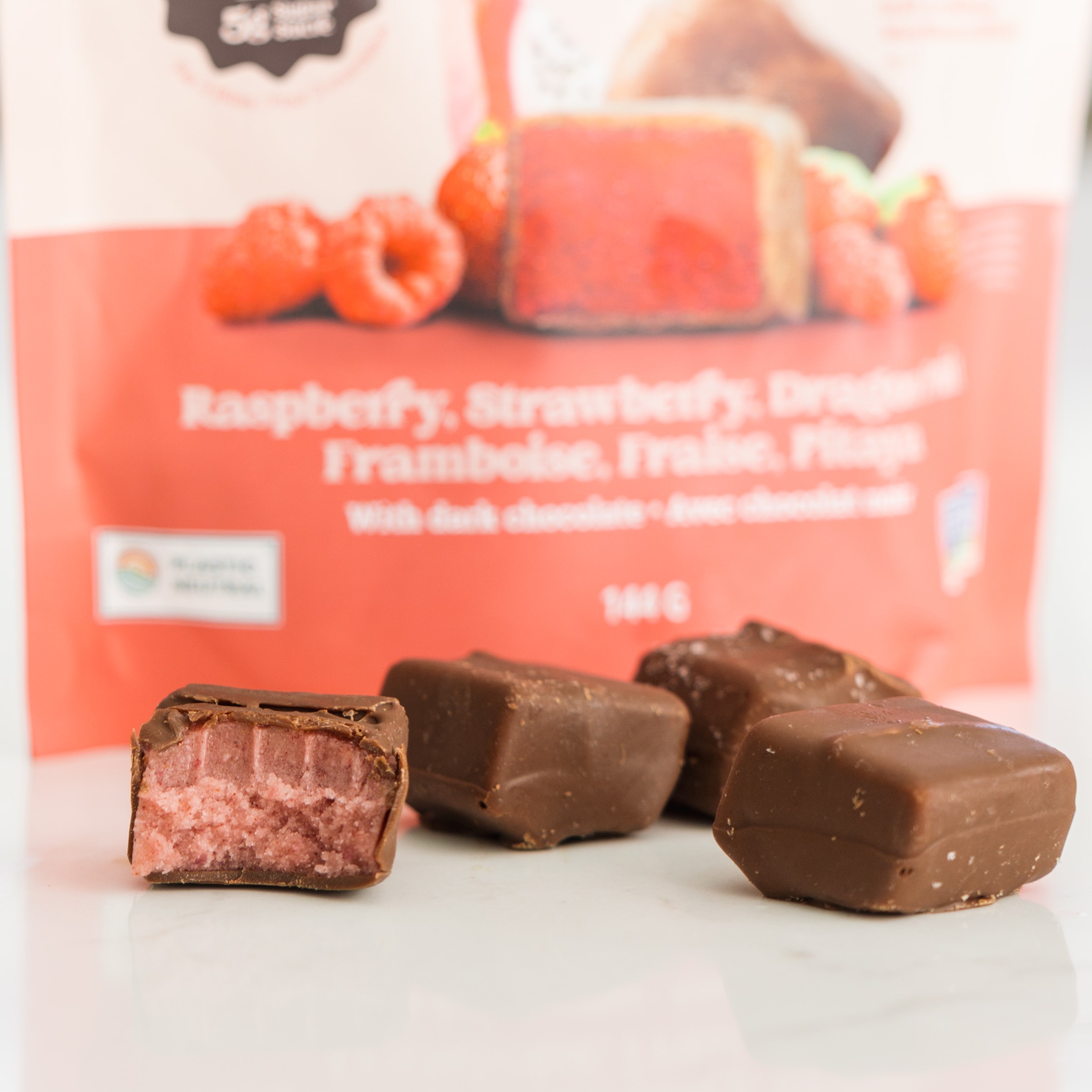 Chocolate-covered fruit pieces with a raspberry filling, in front of a product package.
