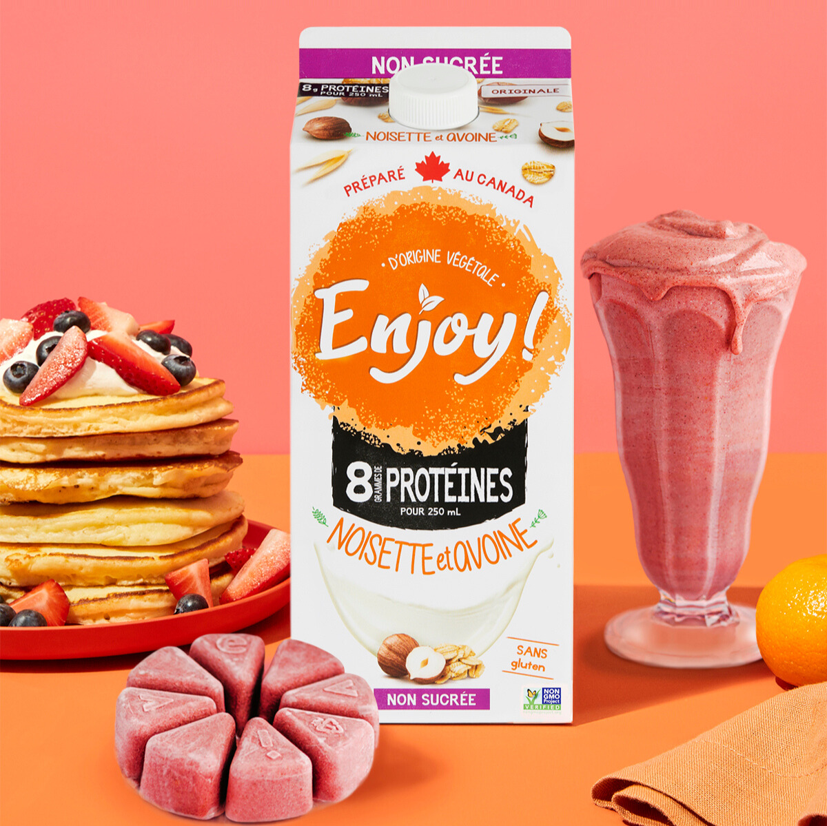 Carton of plant-based protein drink with pancakes, smoothie, and fruit on a colorful background.