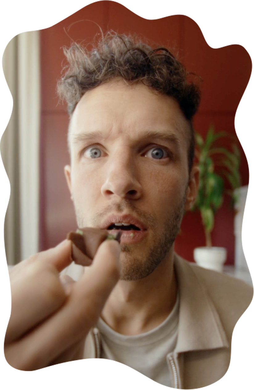 A man with bright green eyes looks surprised as he is about to eat a piece of chocolate.