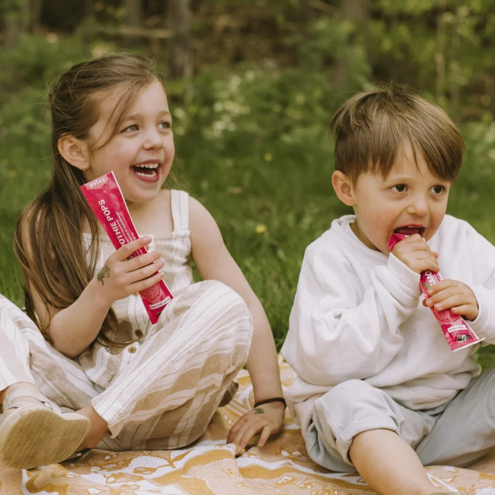 Two children sitting on a blanket, enjoying frozen treats outdoors.