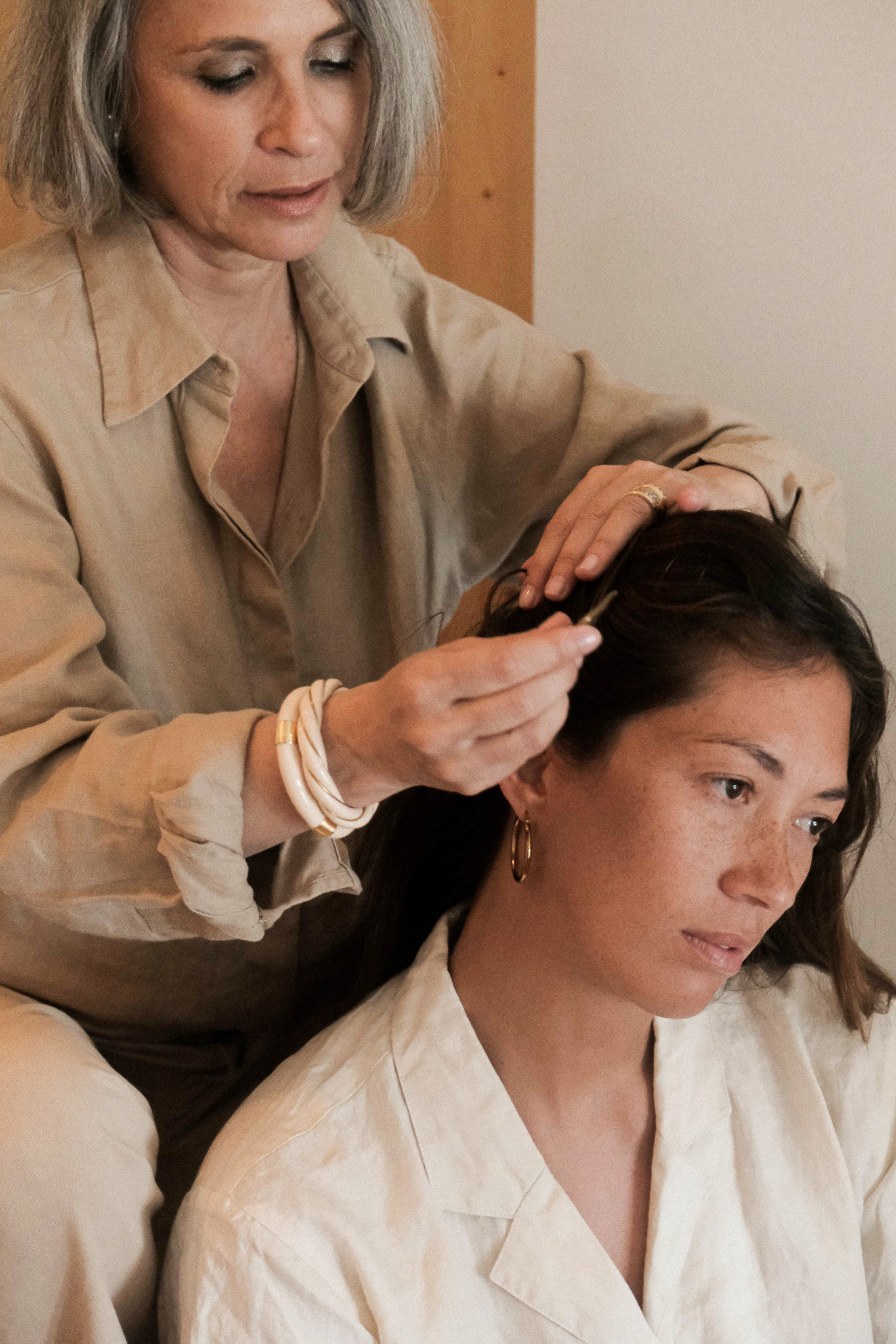 A woman styles another woman's hair indoors.