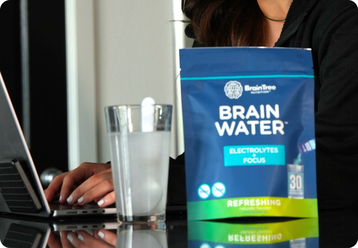 Person using a laptop with a glass and Brain Water package on the table.