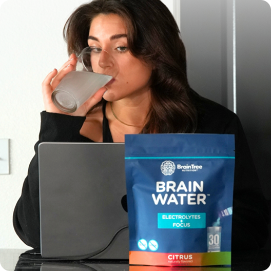 Person drinking from a glass, with a Brain Water package in front.
