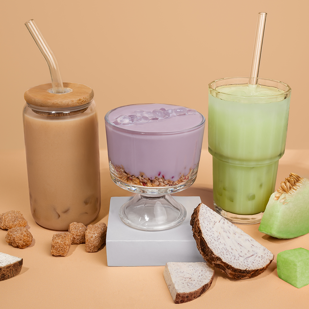 Three drinks with glass straws, surrounded by fruit and sugar cubes on a beige background.