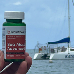 A hand holds a bottle of Sea Moss Advanced near a boat on the water.