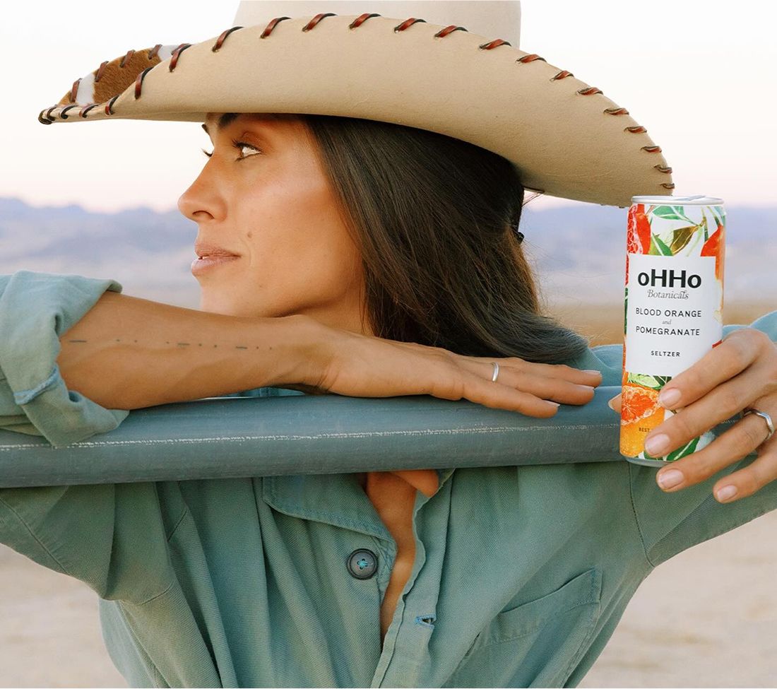 Person in a cowboy hat holding a can of oHHo Botanicals seltzer.