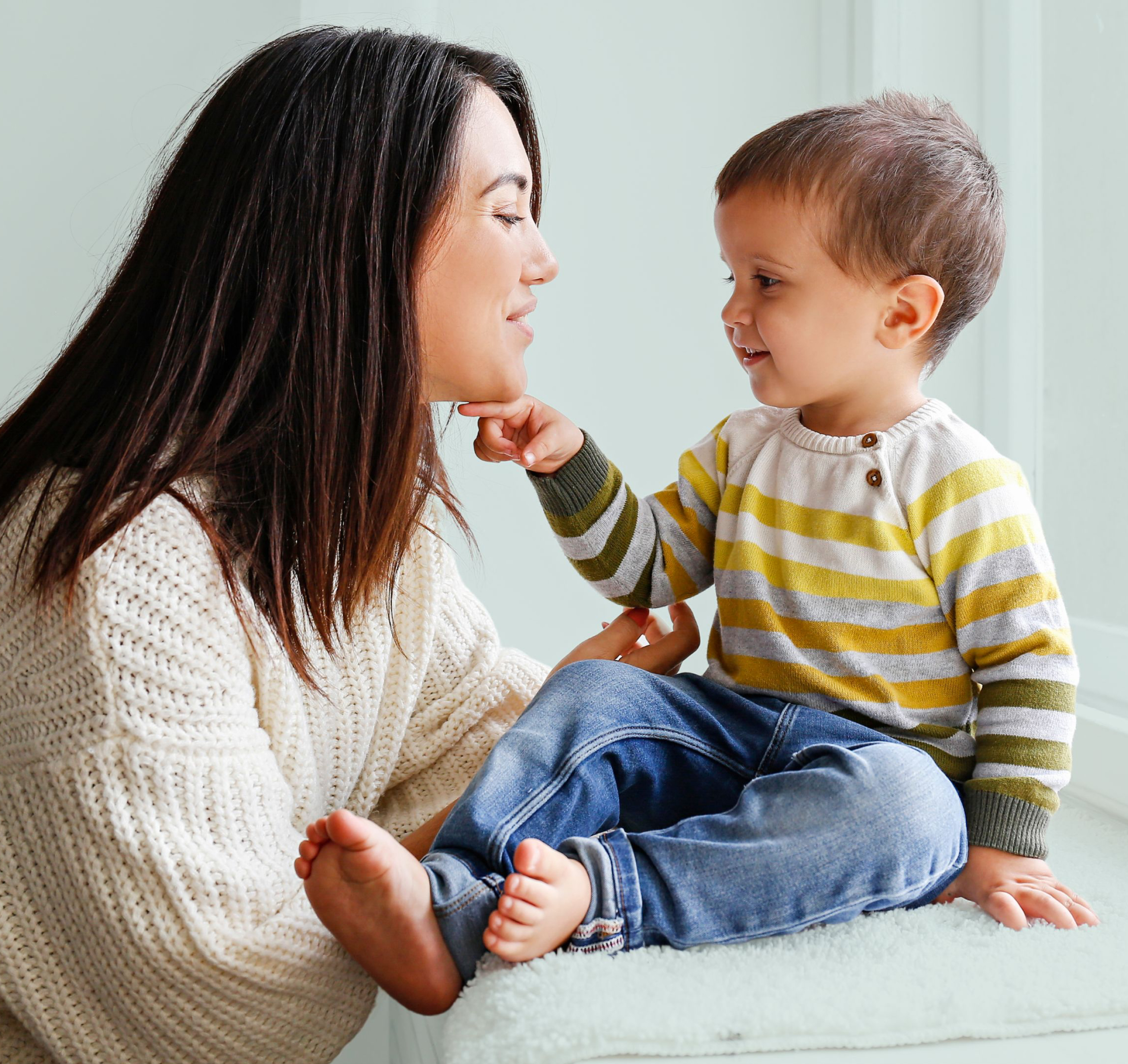 Woman and child smiling at each other indoors.