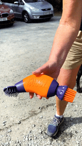 Person holding an orange and purple pet grooming tool with brush attachment.