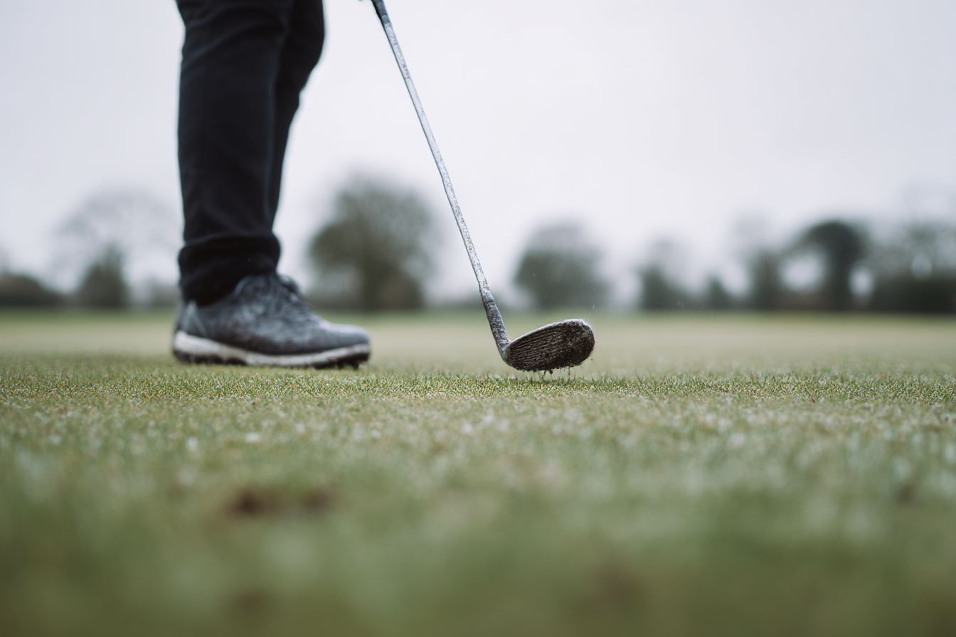 Person's lower legs with a golf club on a grassy field.