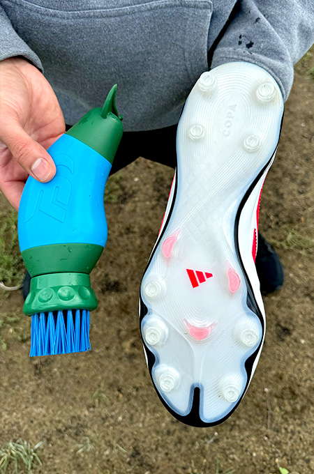 Person holding a cleat and a cleaning brush in their hands.