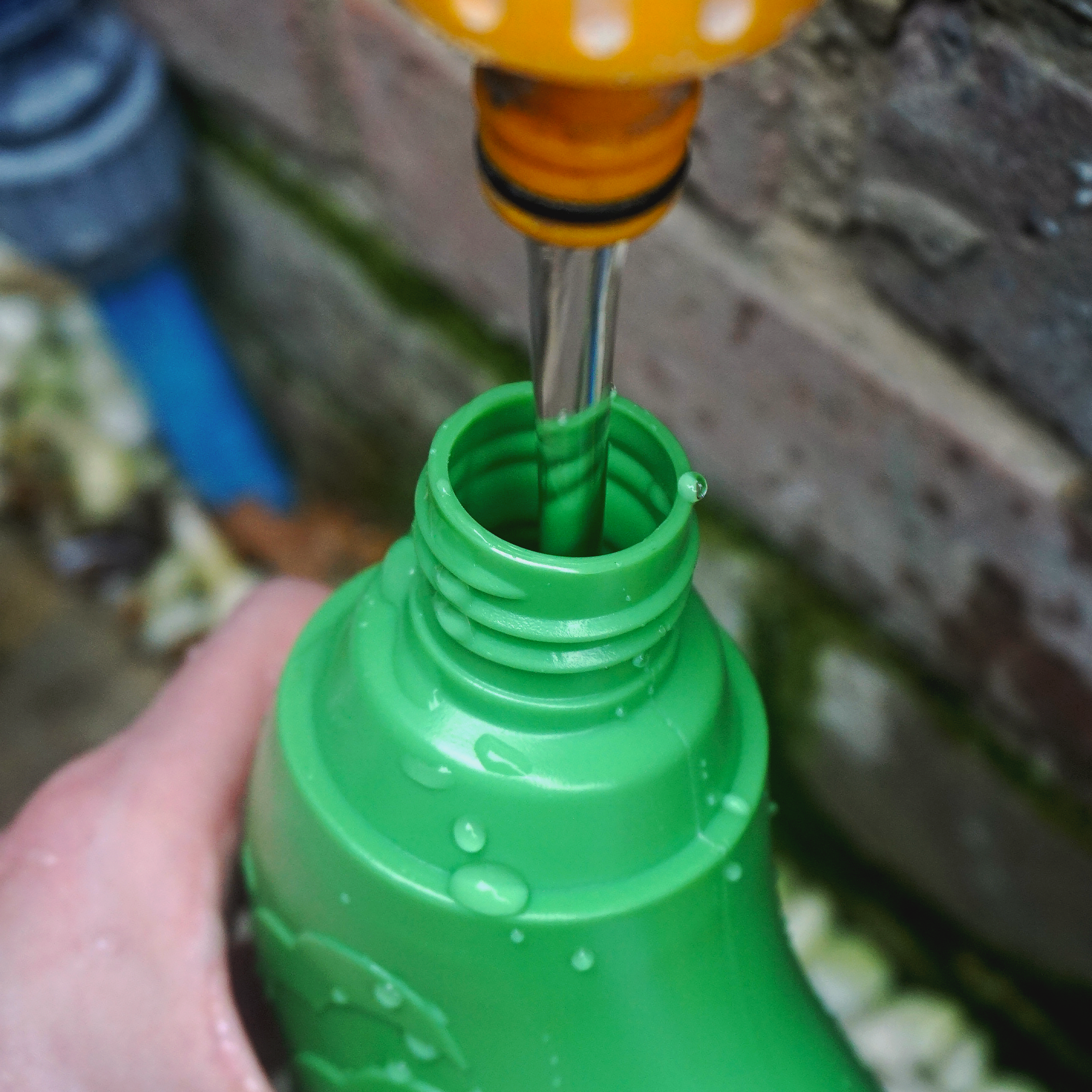 Green bottle being filled with water from a hose.