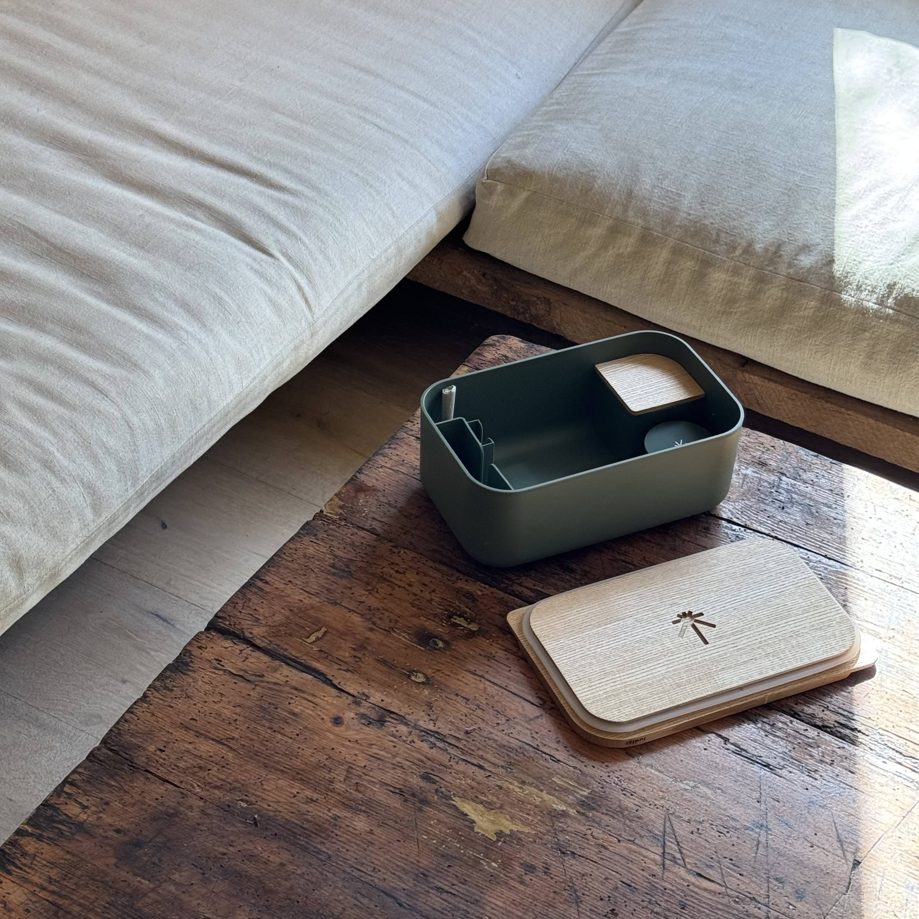 An open, olive green storage box with a wooden lid sits on a rustic wooden coffee table.
