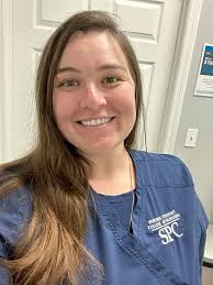 Person smiling in blue scrubs with white door background.