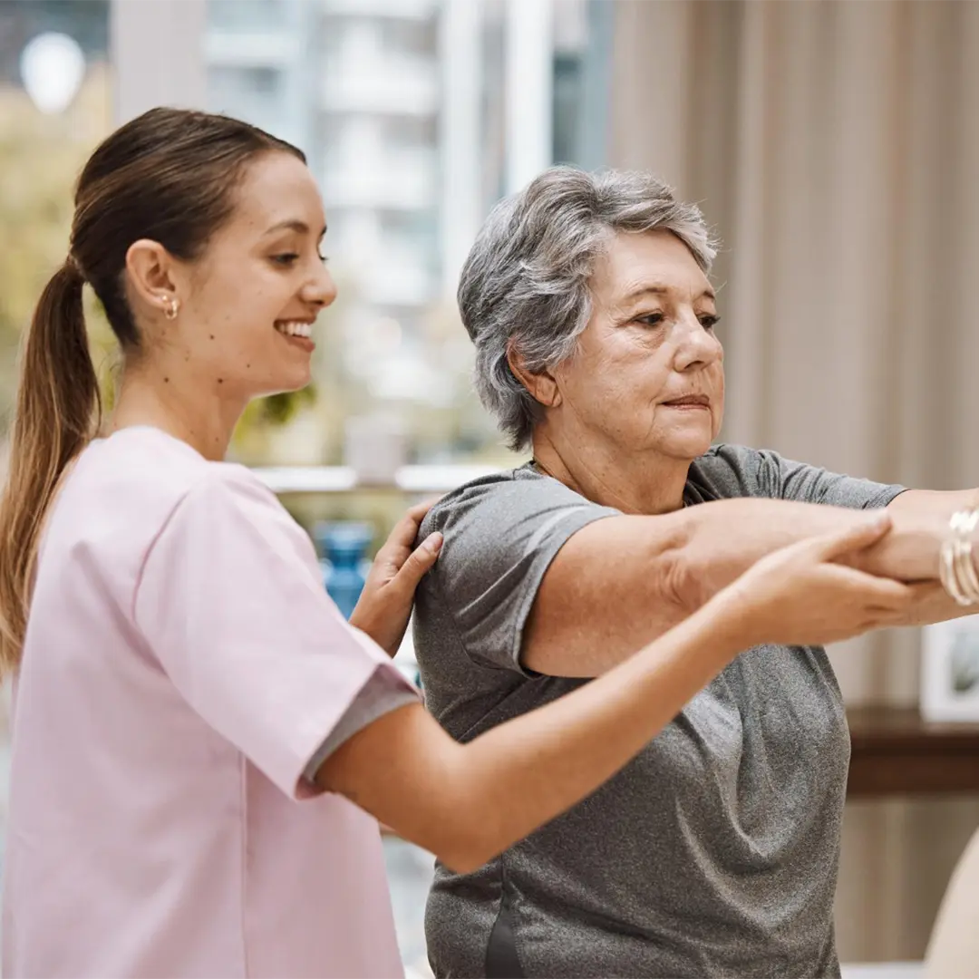 A caregiver assists an elderly woman with a stretching exercise.
