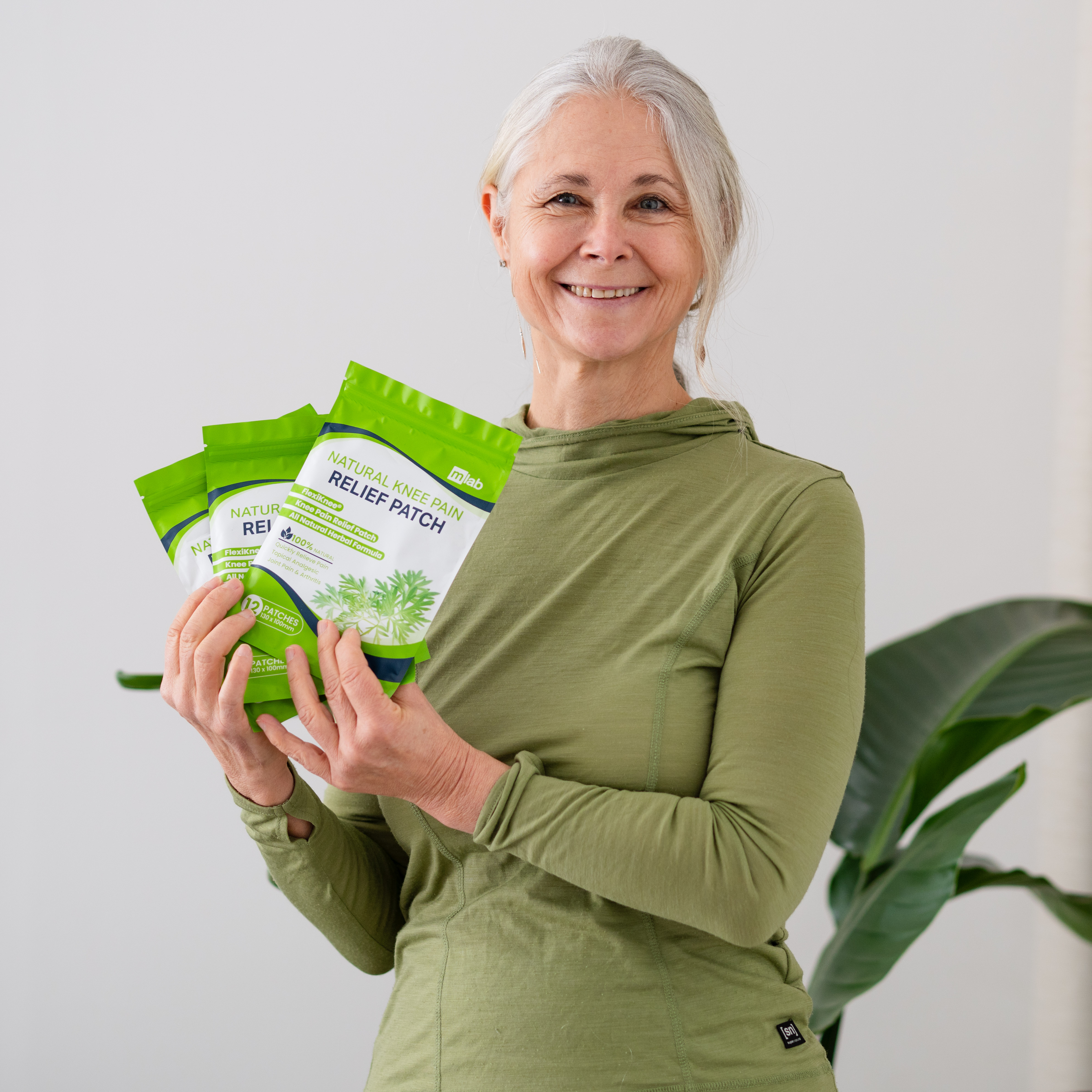 Person holding green knee pain relief patch packages, smiling.