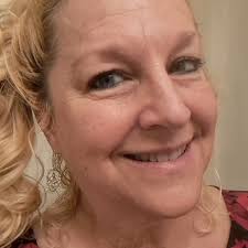 A close-up photo of a smiling, middle-aged woman with blonde hair and blue eyes.
