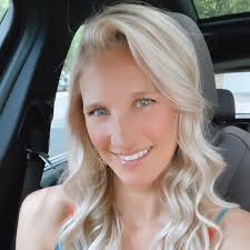 A smiling person with long blonde hair sitting in a car.