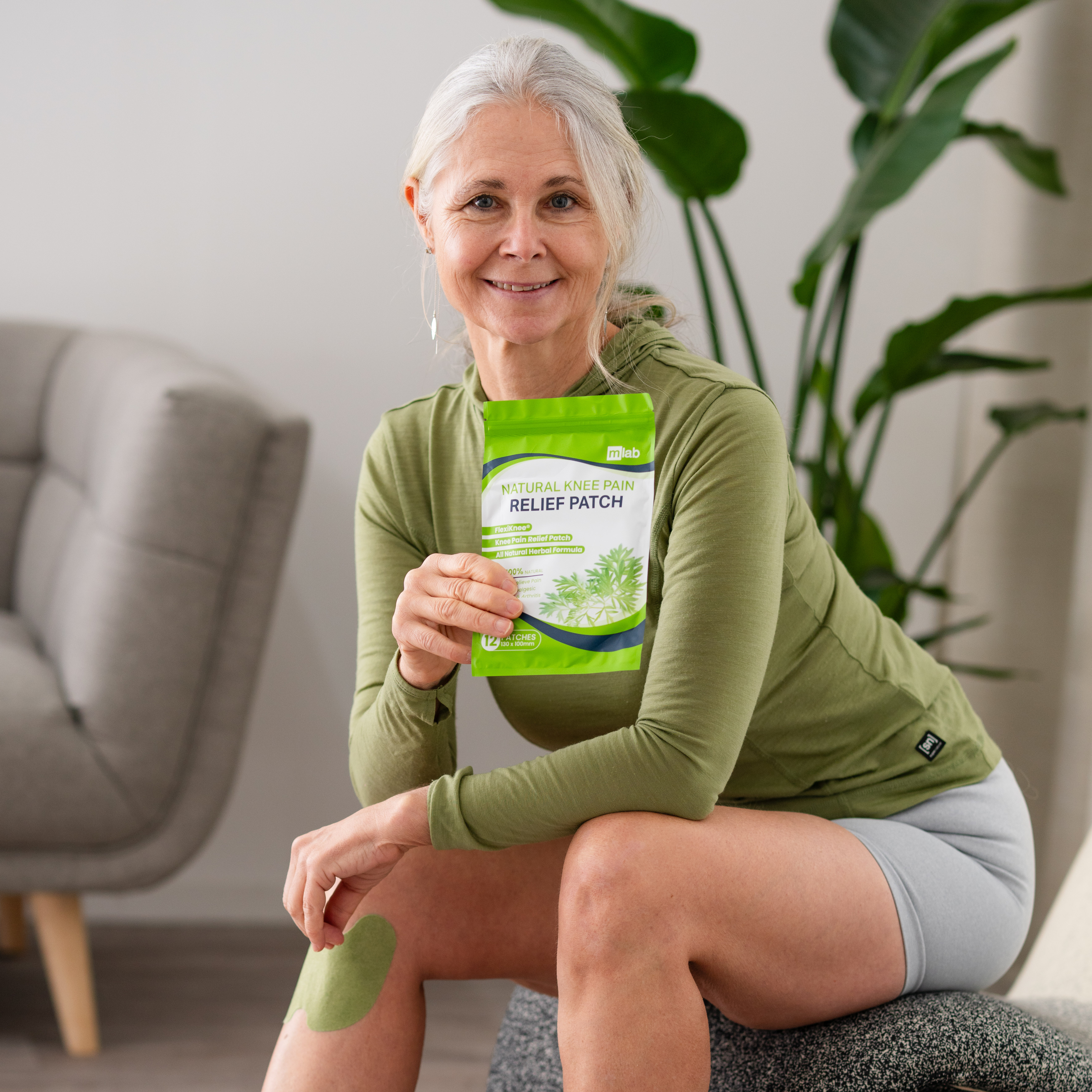 Woman holding a knee pain relief patch package, sitting on a couch.
