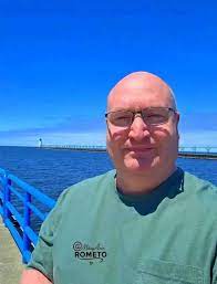 Person in green shirt standing on a pier with a lighthouse in the background.