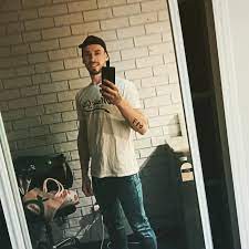 Person taking a mirror selfie in a room with a brick wall backdrop.