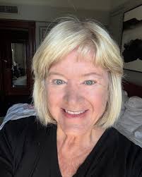 A close-up photo of a smiling, middle-aged woman with blonde hair and blue eyes.